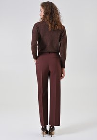 Maglione marrone scintillante in maglia abbinato a pantaloni aderenti bordeaux. Presenta un dettaglio con tasca posteriore e eleganti tacchi neri lucidi.