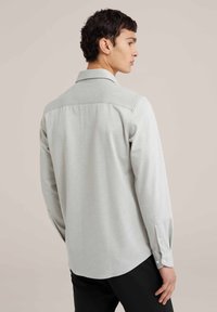 Lichtgrijze longsleeve shirt met een puntige kraag, textuurstof, knoopmanchetten en een afgeronde zoom, gedragen met zwarte broek.