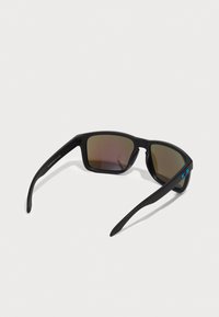 Schwarze rechteckige Sonnenbrille mit Verlaufsgläsern, matte Oberfläche und blauem Logo-Akzent an der Seite. Leichter Kunststoffrahmen.