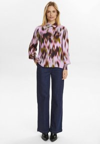 En button-up skjorta i abstrakt mönster med rosa, bruna och gröna nyanser, långärmad med samlade manschetter; ihop med vida mörka denimjeans och svarta stövlar.