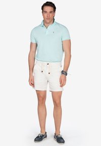 Camisa polo de color azul claro con mangas cortas, combinada con pantalones cortos blancos. El calzado consiste en zapatos de barco de color azul oscuro, que cuentan con cordones y acentos blancos.