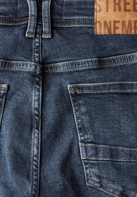 Jeans de mezclilla azul marino con una cintura alta, dos bolsillos traseros y una etiqueta de cuero marrón con texto embossado.