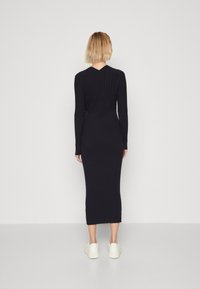 Marineblaues, geripptes Midikleid mit langen Ärmeln, V-Ausschnitt hinten und taillierter Silhouette. Kombiniert mit weißen Sneakers, minimalistisches Design.