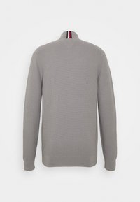 Maglione grigio con texture a coste, colletto alto con una striscia rossa e navy. Maniche lunghe e orlo aderente in vita. Vista posteriore.