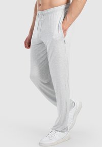Hellgraue Sweatpants aus einem weichen Stoff, ausgestattet mit einem Kordelzugbund und Seitentaschen, kombiniert mit weißen Turnschuhen.