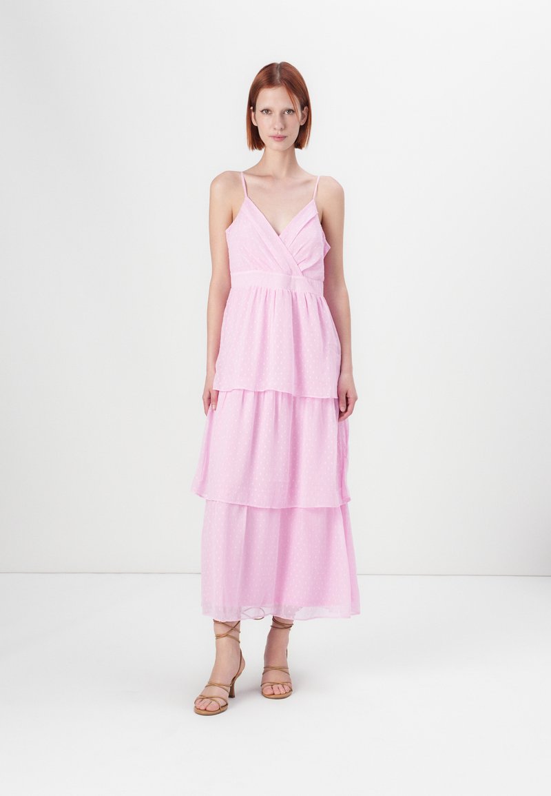 Lyserød tiered maxi kjole med spaghetti stropper, der har en indviklet bodice og en prikket tekstur, parret med brune stiletter.