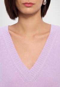 Maglione lavorato a maglia color lavanda con scollo a V, caratterizzato da dettagli a coste intorno al colletto. Texture liscia, spessore medio e linee pulite.