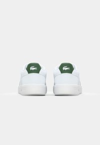Witte sneakers met een gladde leren afwerking, groene hielaccenten en een logo-detail op de achterkant. Beschikt over een lage ontwerp en een gestructureerde zool.