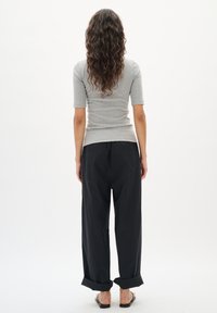 Cămașă gri cu model în dungi, cu mâneci scurte, asortată cu pantaloni negri largi, puțin rulați la manșete, purtați cu sandale negre.