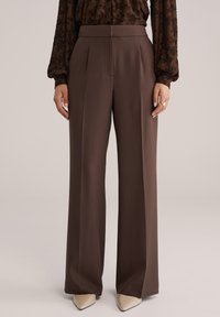 Pruunid laia lõikega püksid, volditud, valmistatud viimistletud kangast. Disainil on kõrge vöökoht ja sile tekstuur.