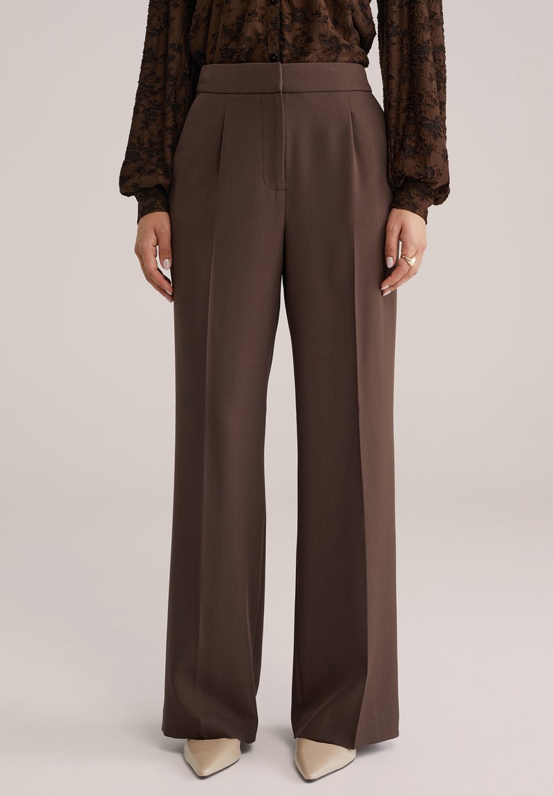 Pruunid laia lõikega püksid, volditud, valmistatud viimistletud kangast. Disainil on kõrge vöökoht ja sile tekstuur.