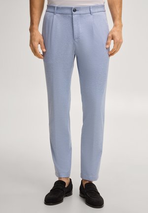 Pantaloni de culoare bleu, texturată, slim fit, purtați cu mocasini negri din piele întoarsă și o cămașă albă băgată în pantaloni, prezentată de la talie până la picioare.