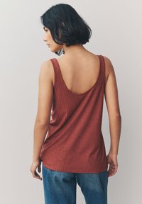 Débardeur couleur rouille avec un dos en forme de cœur, texture côtelée et larges bretelles. Associé à un jean en denim bleu clair, mettant en valeur une coupe décontractée.