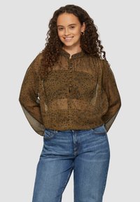 Braune, gemusterte Bluse mit einer Knopfleiste, hohem Kragen und durchsichtigen Ärmeln. Kombiniert mit blauen Jeans in lässiger Passform.