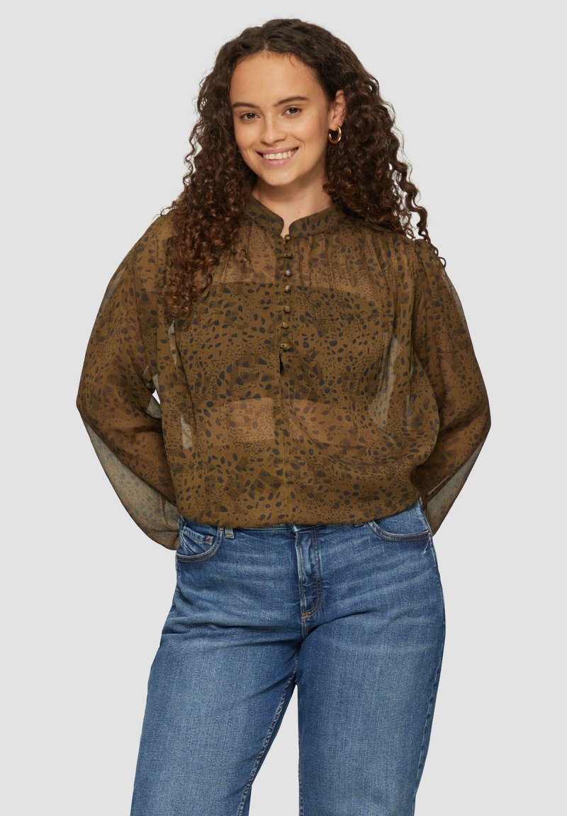 Braune, gemusterte Bluse mit einer Knopfleiste, hohem Kragen und durchsichtigen Ärmeln. Kombiniert mit blauen Jeans in lässiger Passform.