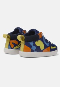 Zapatos infantiles coloridos en azul marino, con un patrón abstracto multicolor, suela blanca y acentos amarillos en la lengüeta del talón.