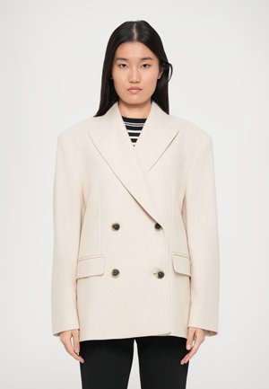 Beige dobbeltradet blazer lavet af tekstureret stof, med sorte knapper og to frontlommer, designet med en afslappet pasform og brede klapper.
