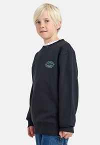 Mørk grå sweatshirt med ribbet hals og ermer, med et lite blått og grønt logo-merke på brystet. Myk stoffoverflate.
