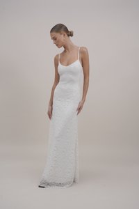 Rochie maxi albă din dantelă cu bretele subțiri, având o siluetă ajustată, modele florale și o ușoară trenă la tiv. Textură netedă.