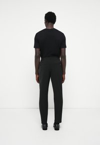 Svart t-shirt och svarta byxor, slim fit, slät tyg, rak skärning, med två bakfickor, bärs med mörka skor.