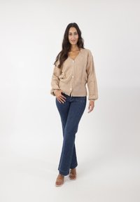 Beżowy sweter z dzianiny z fakturowanym wykończeniem i guzikami, połączony z ciemnoniebieskimi dzwonami i przezroczystymi sandałami na paski.