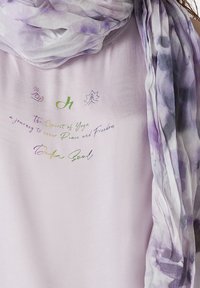 Lyse lilla tørklæde med et flydende design, der har et tie-dye mønster i mørkere lilla nuancer. Teksten inkluderer sætninger relateret til yoga og fred.