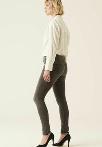 Camisa blanca de botones, jeans gris ajustados, zapatos de tacón negro; el perfil lateral muestra un diseño ajustado y una textura de tela suave.
