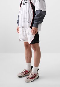 Athletic outfit featuring a white and black shirt with signatures, matching shorts, and sleek gray and red sneakers with textured laces.