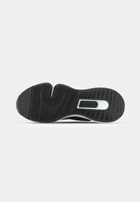 Semelle d'une chaussure de sport noir et blanc montrant des motifs de grip texturés et un logo visible dans la zone du talon.