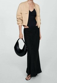 Beżowa krótka kurtka, czarna top bez rękawów, długa czarna spódnica i czarna torebka w kształcie półksiężyca. Dopełnieniem stroju są czarne płaskie sandały.