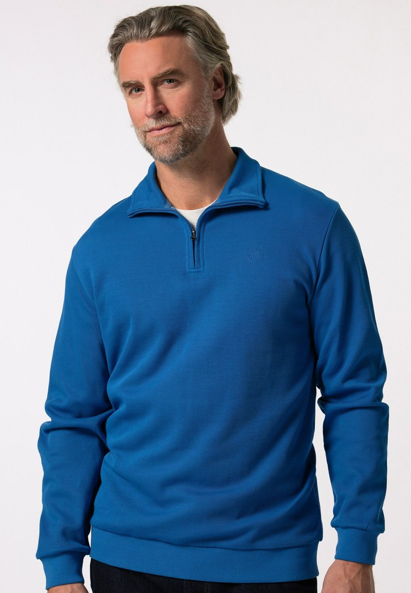Modrý svetr s límcem na zip, ribbovanou texturou, dlouhými rukávy a přiléhavým páskem. Na hrudi má decentní logo.