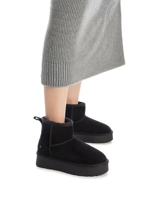 Botines de ante negros con puntera redonda, forro suave y suela texturizada. Cuenta con una pestaña lateral para tirar y una marca de acento en la parte posterior.
