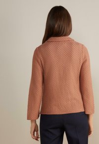 Texturovaná, světle korálová bunda s límcem, tříčtvrtečními rukávy a přiléhavým střihem, prezentována zezadu na neutrálním pozadí.