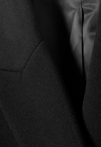 Dark textured wool coat overlapping a smooth satin-like fabric, showing contrast between matte and shiny materials in close-up detail.