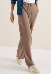 Beige sweatpants met een elastische tailleband, trekkoorddetails en zijzakken, gecombineerd met lichtgekleurde sneakers.