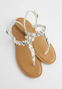 Witte leren teensandalen met een flat bruine zool, voorzien van een decoratieve zilveren edelsteenaccent op de band. Verstelbare enkelgesp.