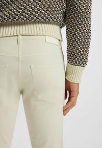 Stickad tröja i brunt och vitt med ribbad nederkant. Ljusfärgade jeans med bakfickor. Slät textur och figurnära design.