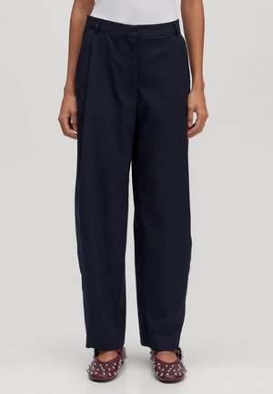 Marineblauwe wijde pijpen broek met een hoge taille, voorzien van voorplooien en een gladde, gestructureerde stof. Gekoeld met versierde bordeauxrode schoenen.