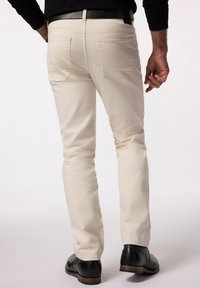 Pantalones de algodón beige con corte ajustado, con bolsillos traseros y una textura suave, combinados con zapatos de piel negra.