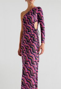 Robe asymétrique avec une épaule dénudée, motifs ondulés rose, noir et or, détail ajouré et lien ajustable sur le côté. Fabriquée dans un tissu texturé.