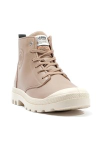 Botte montante beige en cuir lisse avec une semelle en caoutchouc texturé, dotée de lacets, d'un écusson de logo et d'un bout de chaussure blanc contrastant.