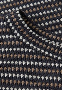 Tissu tricoté plié, présentant un motif répétitif de petits losanges en fils blancs, beige et gris foncé.