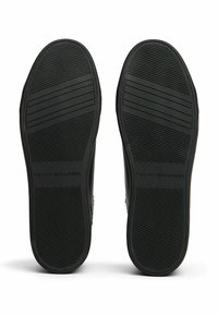 Suole di scarpe in gomma nera con modelli di battistrada orizzontali e verticali, con il logo "Tommy Hilfiger" impresso vicino al tallone.