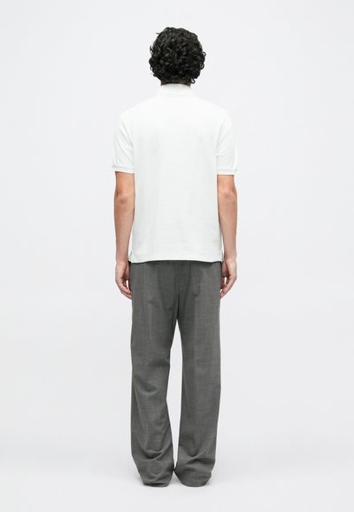 Biele polo tričko s krátkymi rukávmi v kombinácii so sivými, voľne padnúci nohavicami, ktoré prezentujú hladkú textúru a jednoduchý dizajn z pohľadu zozadu.