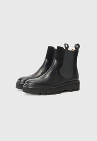 Bottines noires en cuir avec des panneaux élastiques sur les côtés, des accents en suede texturé, des anses de tirage et une semelle en caoutchouc épaisse avec un motif de crampons.