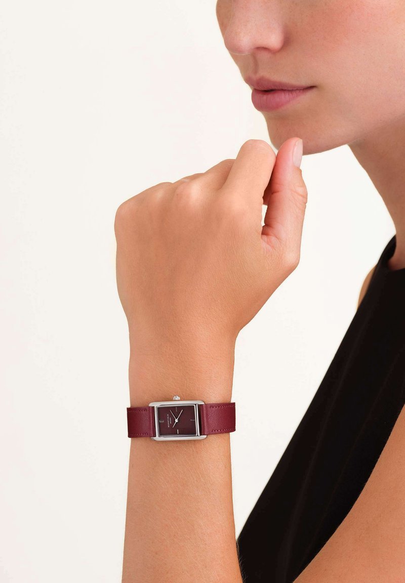 Orologio analogico rettangolare con cinturino in pelle rossa scura, hardware in argento e quadrante nero minimalista con indicatori delle ore bianchi.