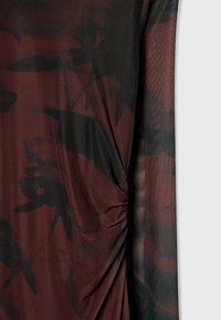 Tissu transparent rouge foncé avec imprimé floral noir, avec un détail de drapé froncé d'un côté.