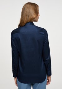 Camicia in satin blu navy con maniche lunghe, colletto a punta e polsini con bottoni; texture liscia e orlo curvo sul retro.