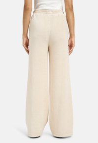 Beige weite Cordhosen mit einem elastischen Bund, die über eine vertikale Rippstruktur und eine glatte Oberfläche verfügen.