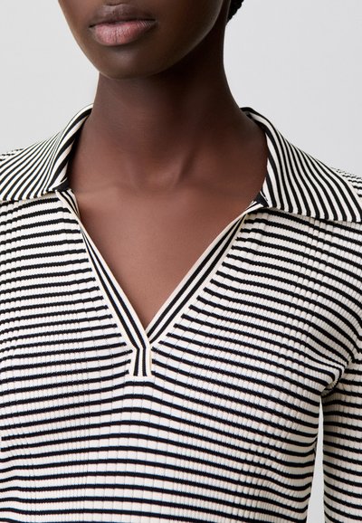 Top a rayas con franjas negras y blancas, cuello en V y textura acanalada, destacando un diseño estructurado.
